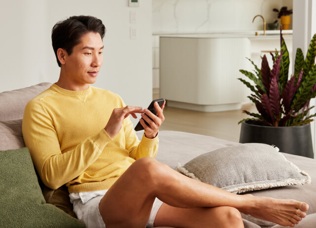 Man sitting on the couch, checking therapy plans from Mosh on his phone